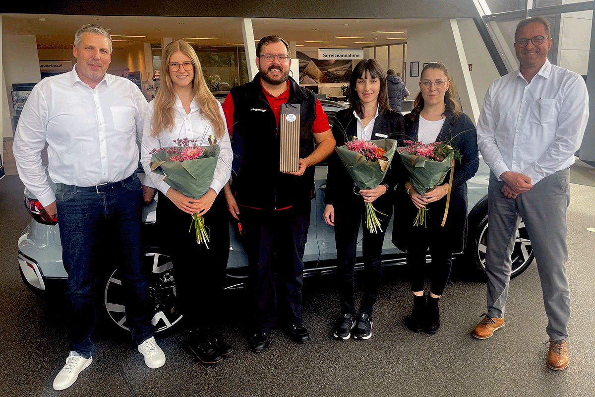 Unsere Serviceleiterin Maria Hainz, Serviceberaterin Rebecca Kofler, Werkstattleiter Benjamin Kürzinger sowie die Serviceassistentinnen Ramona Müller stehen mit Blumensträußen und einer Auszeichnung mit Herrn Stiglmayr und Herrn End im Audi Terminal.