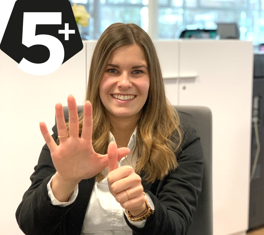 Mitarbeiterin zeigt mit ihrer Hand ein 5+ Zeichen