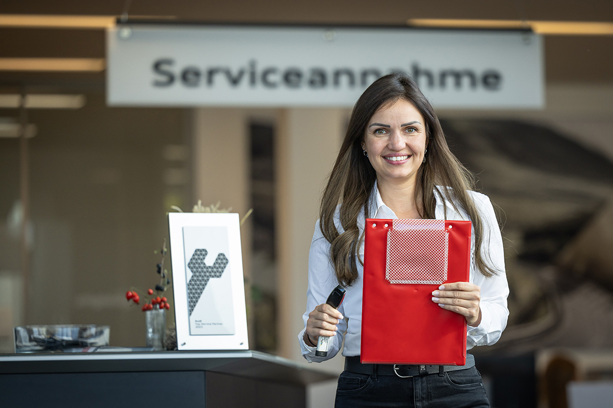Mitarbeiterin mit Klemmbrett in der Hand strahlt in Kamera
