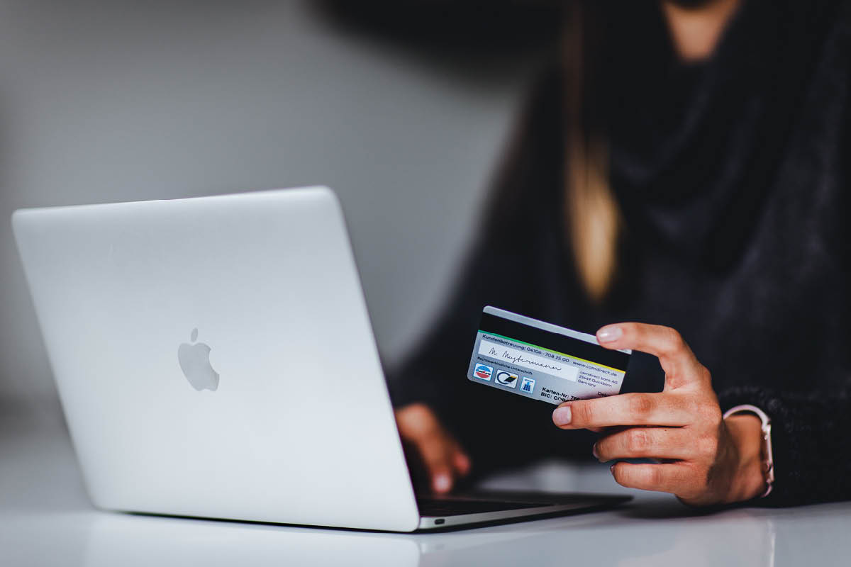 Eine Person tätigt eine Online-Bestellung auf einem Laptop mit einer Karte in der Hand.