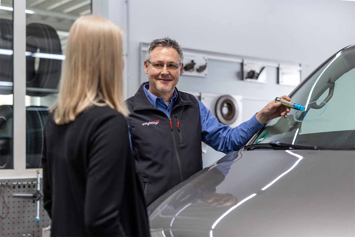 Serviceberater steh mit einer Kundin an der Direktannahme und schaut sich einen Steinschlag an.